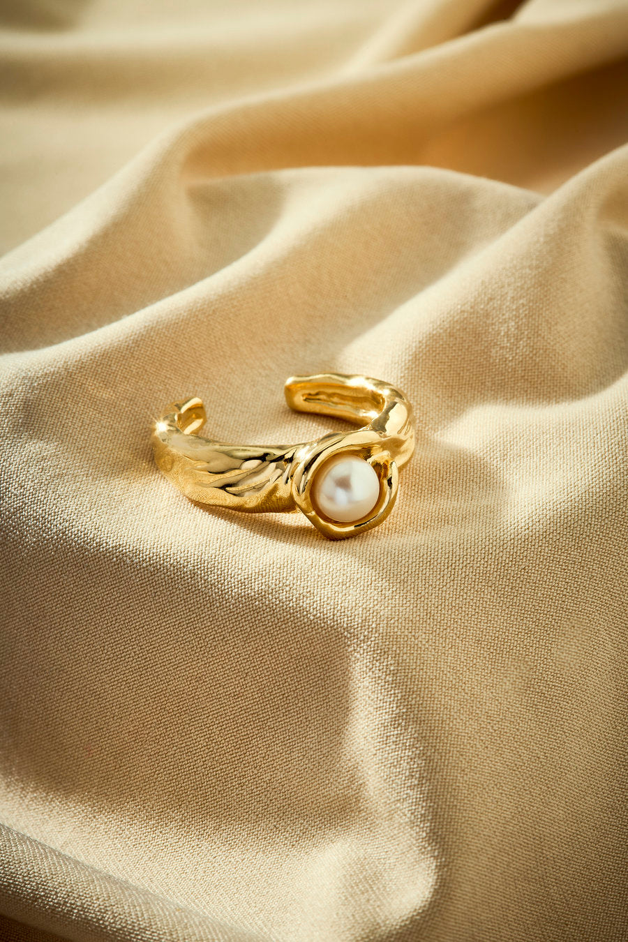 Gold plated ring with a central pearl and textured organic design.