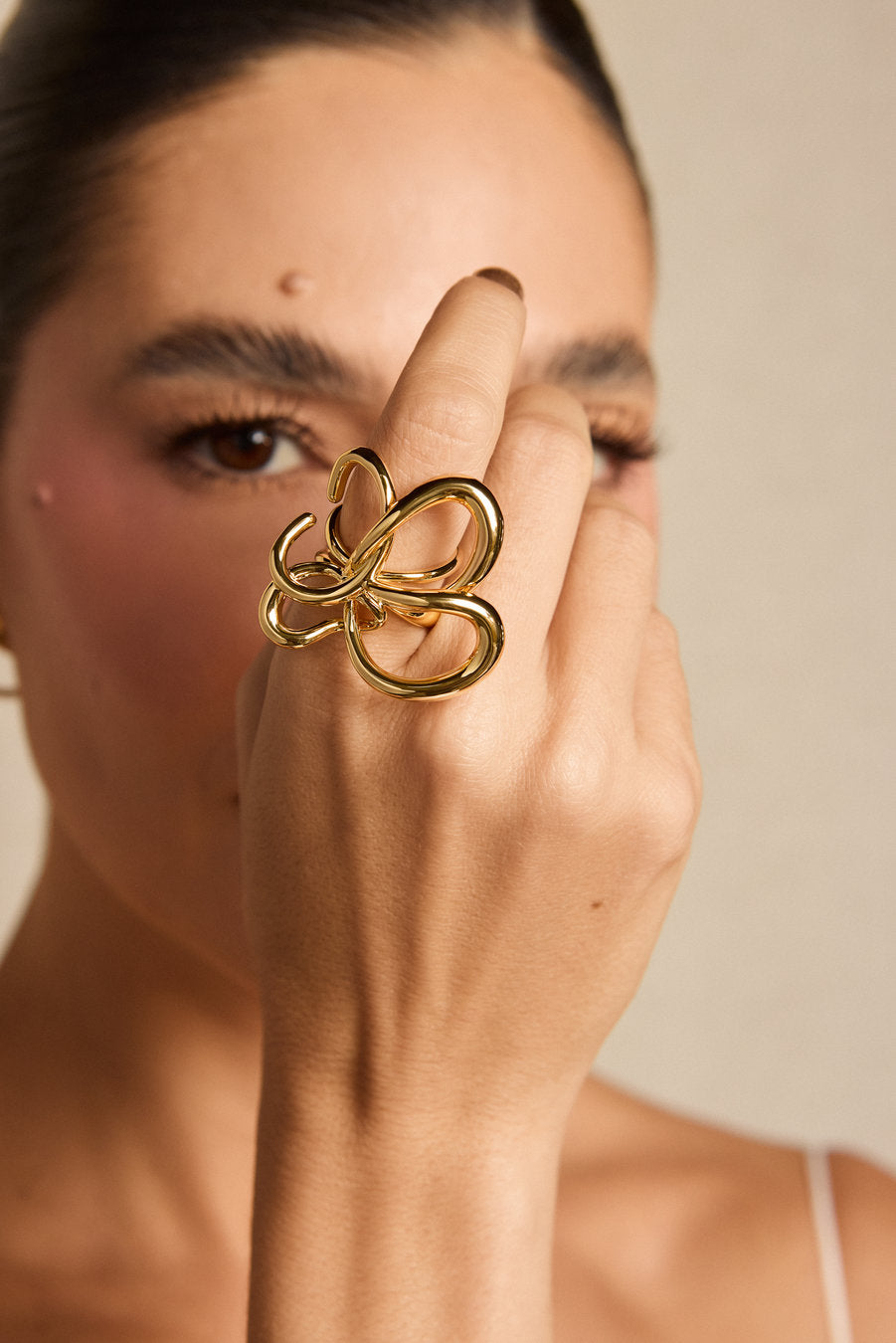 A close-up lifestyle shot of a model wearing a chunky, polished gold ring with an abstract, intertwined loop design on her finger.