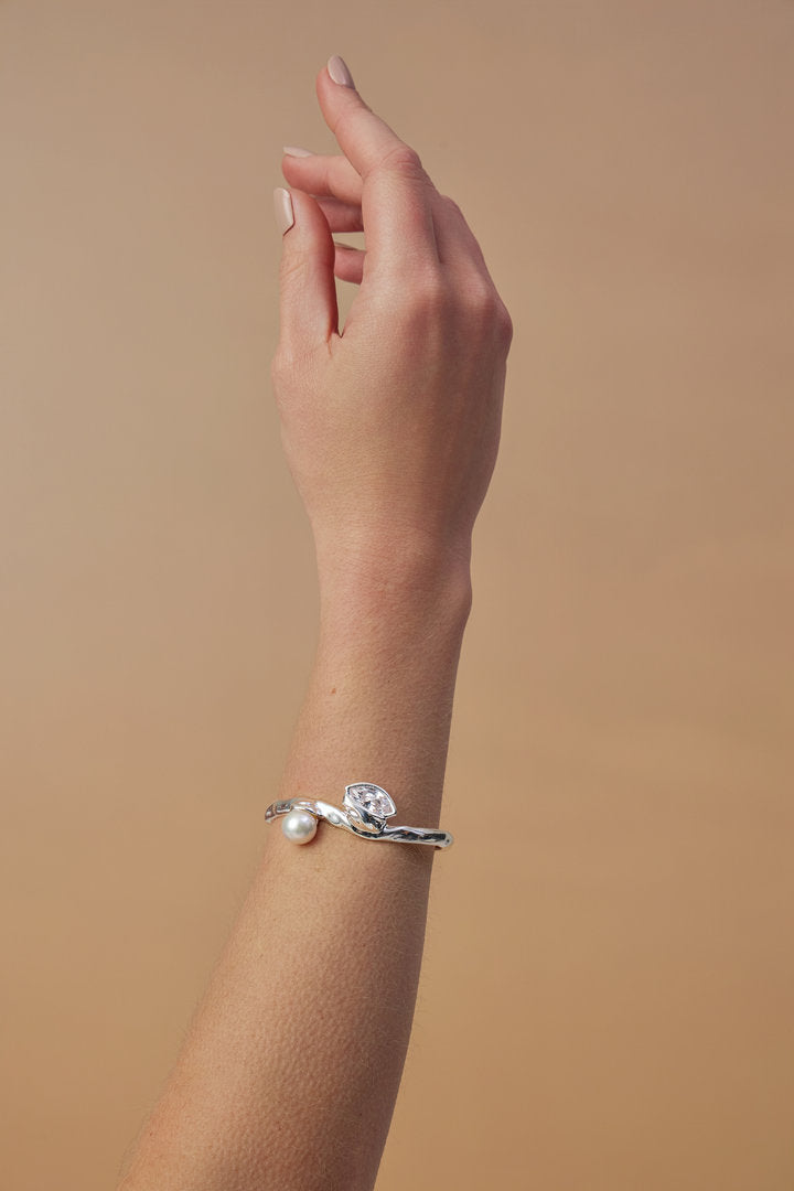 The piece combines contemporary fluidity with traditional jewelry elements, such as the pearl.