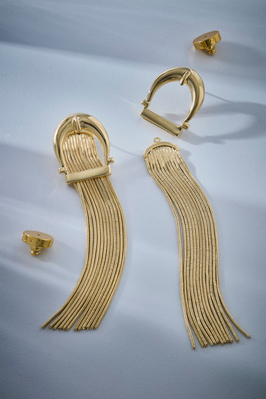 Long gold earring with a sculptural arched top and fringes of fine chains with a polished finish.