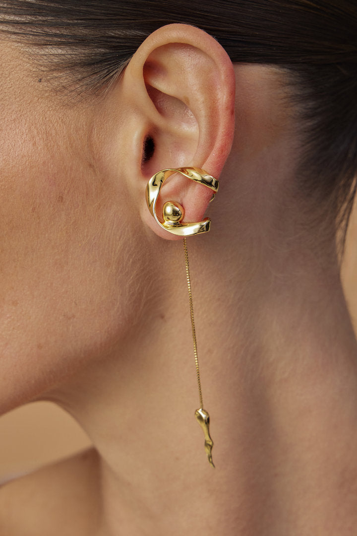 Gold-tone Frida earring featuring a curved structure, long chain, and organic-shaped pendant.