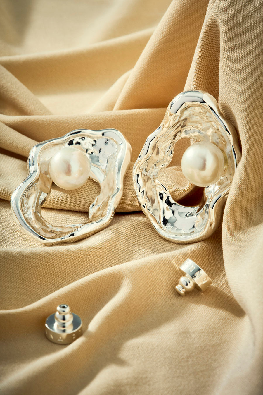 Silver stud earring with a central pearl and an irregular organic design.