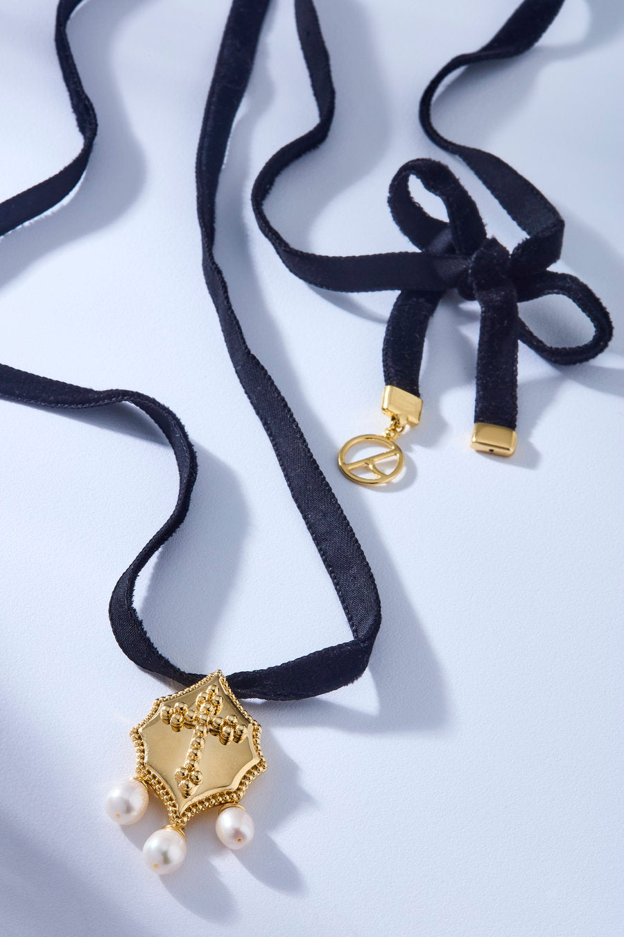 Black velvet choker with a gold shield-shaped pendant, embossed central detail, and three dangling pearls.