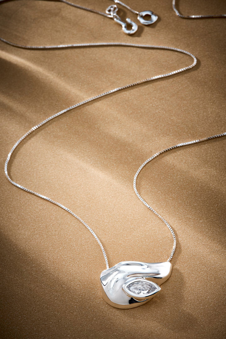 Elsa necklace in silver-tone metal, featuring an organic pendant and a faceted crystal integrated into the design. A sculptural piece exuding effortless, contemporary elegance.