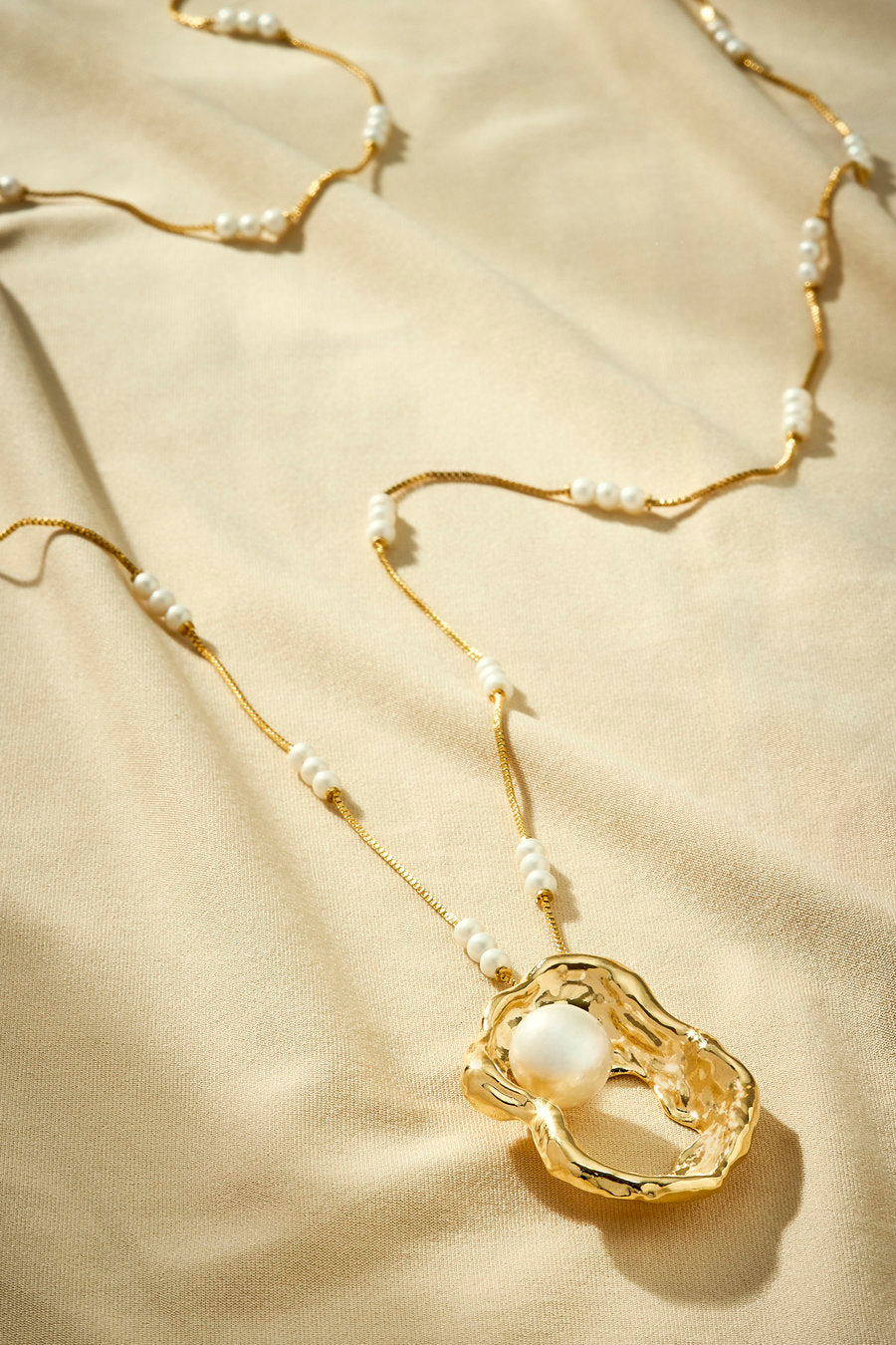 Long gold necklace with pearls and sculptural organic pendant.