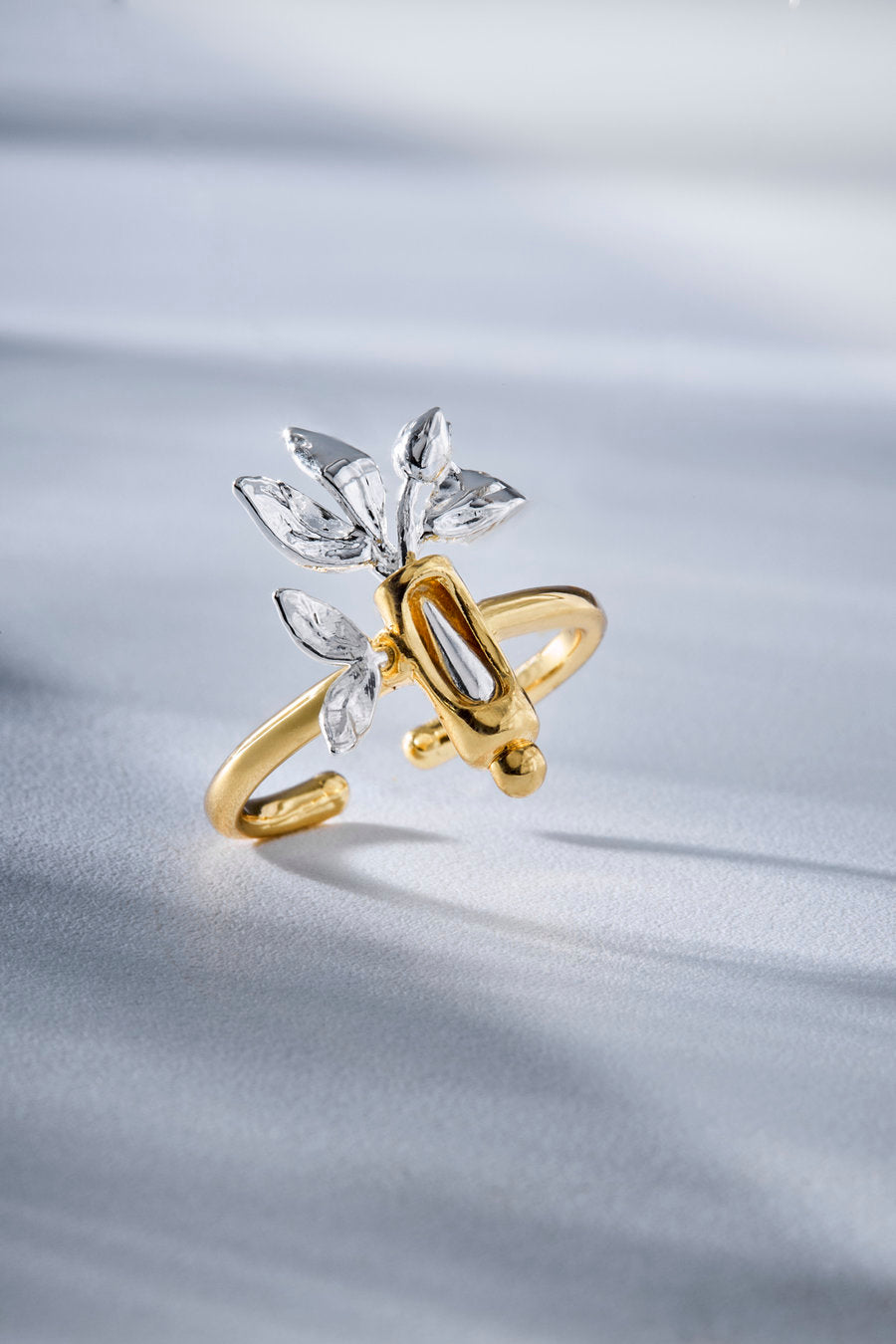A gold and silver ring featuring a stylized bee design with clear crystal leaves, displayed on a soft, light gray fabric background.
