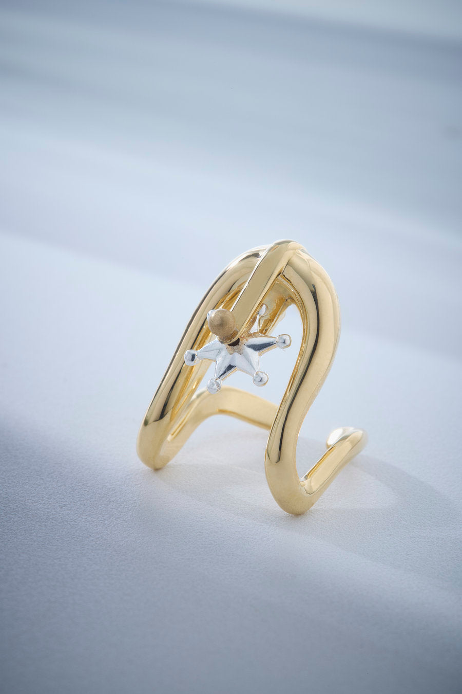 Sculptural gold ring with an open design, organic curves, and a two-tone star-shaped center detail. A statement piece, ideal for conveying strength, sophistication, and self-confidence in striking looks.
