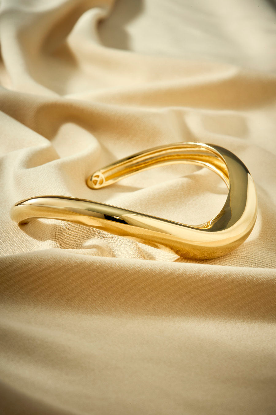 Original gold bracelet with a flowing curve, minimalist aesthetic, and elegant look.