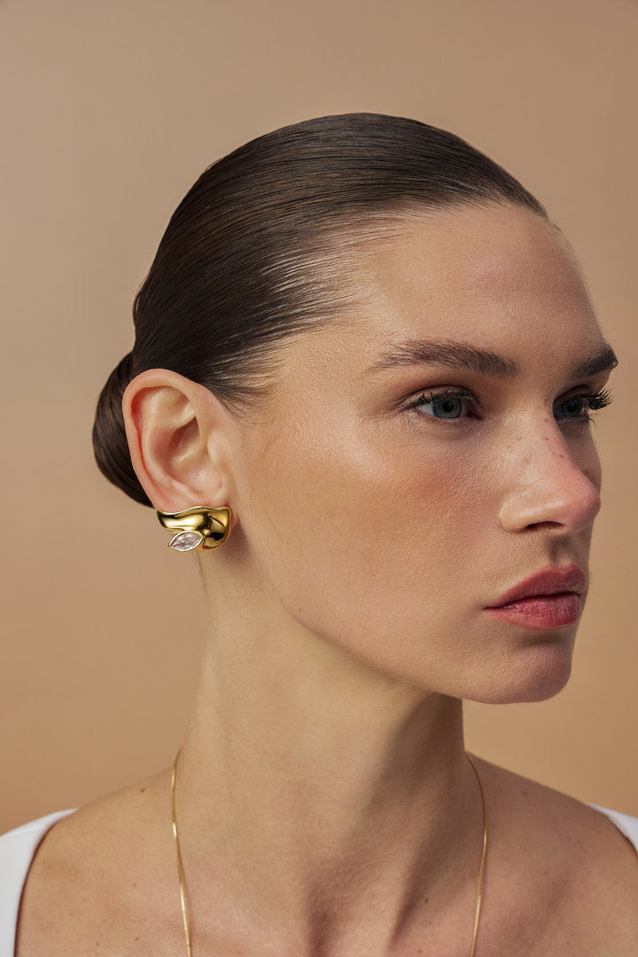 Elsa earring in gold, featuring an organic surface and an Austrian crystal encased in fluid metal. A sculptural, timeless statement piece.