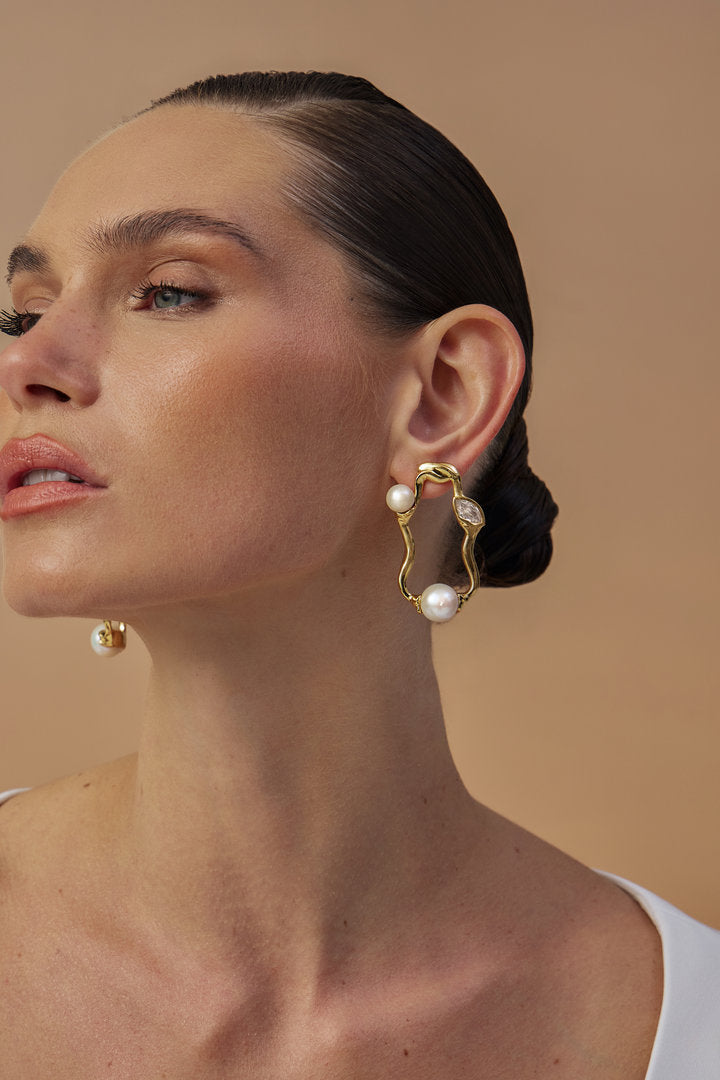 An elegant model is wearing gold-tone Gabrielle earrings featuring organic shapes, pearls, and Austrian crystals.