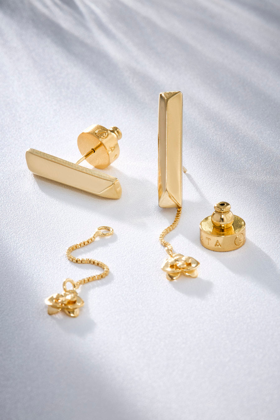 Gold-toned earrings with minimalist lines and a dangling detail, created to express faith, continuous care, and the silent beauty of a love that gives itself entirely.