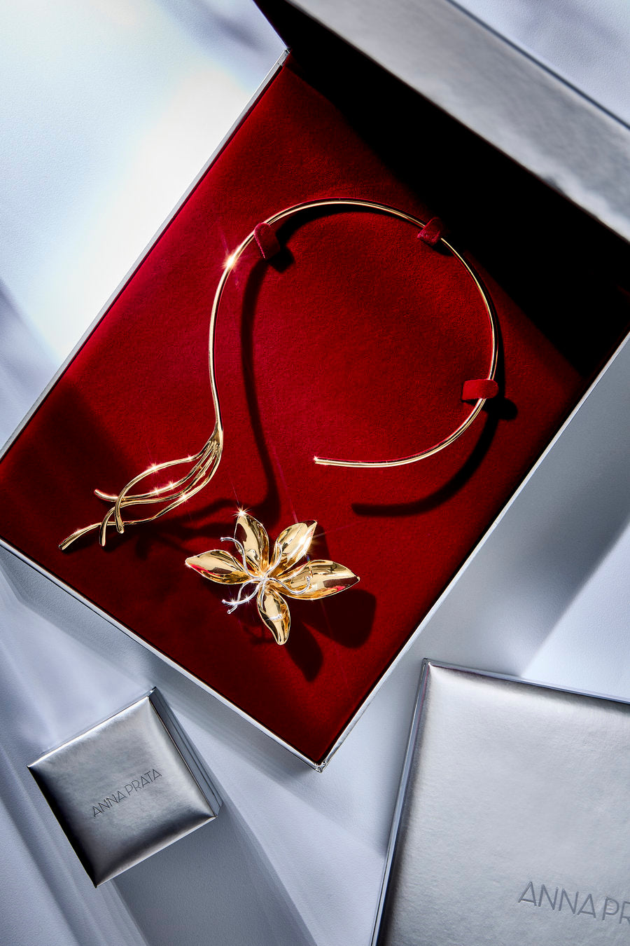 Gold jewelry set by Annarosa, including a delicate gold headband and a matching gold flower-shaped pendant, presented in an open red velvet box with silver packaging.