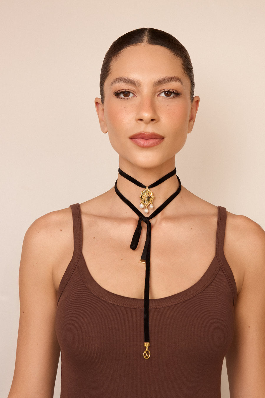 Black velvet choker necklace with gold medallion and dangling pearls, an elegant and striking accessory for the neck.
