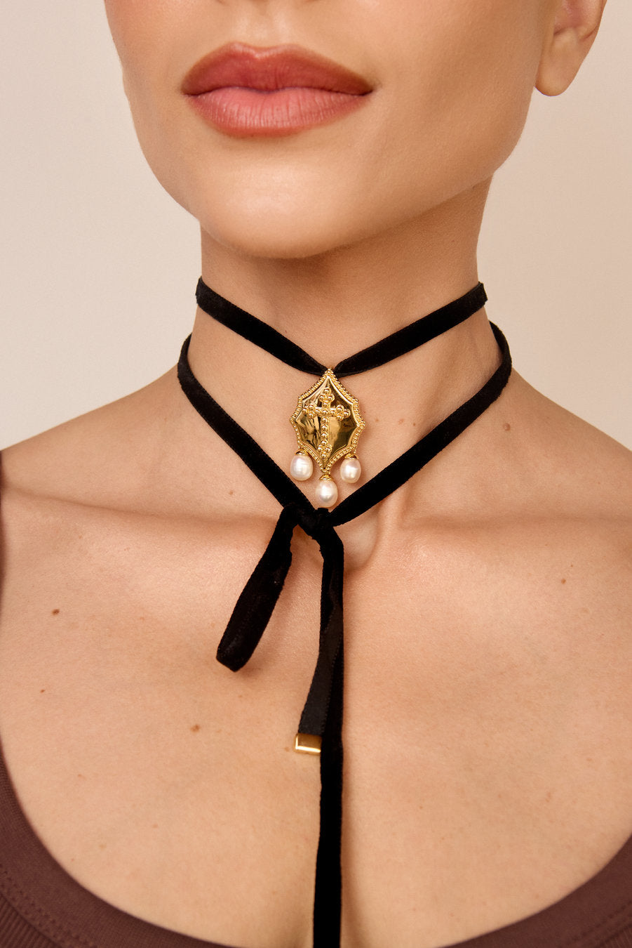 Model wearing a black velvet choker with a gold embossed pendant and pearls, a sophisticated piece of jewelry for elegant looks.
