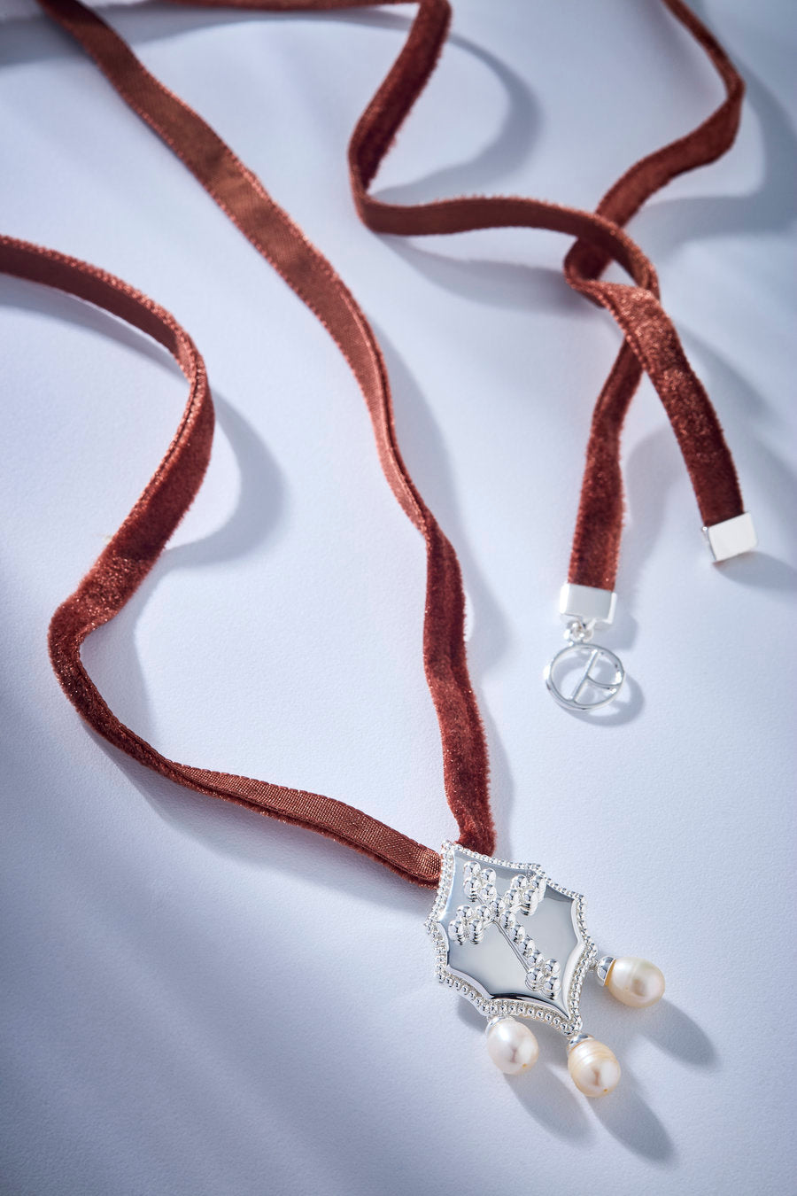 Authority choker with black velvet ribbon, ornamental silver medallion and pearls, ideal for elegant and striking looks.
