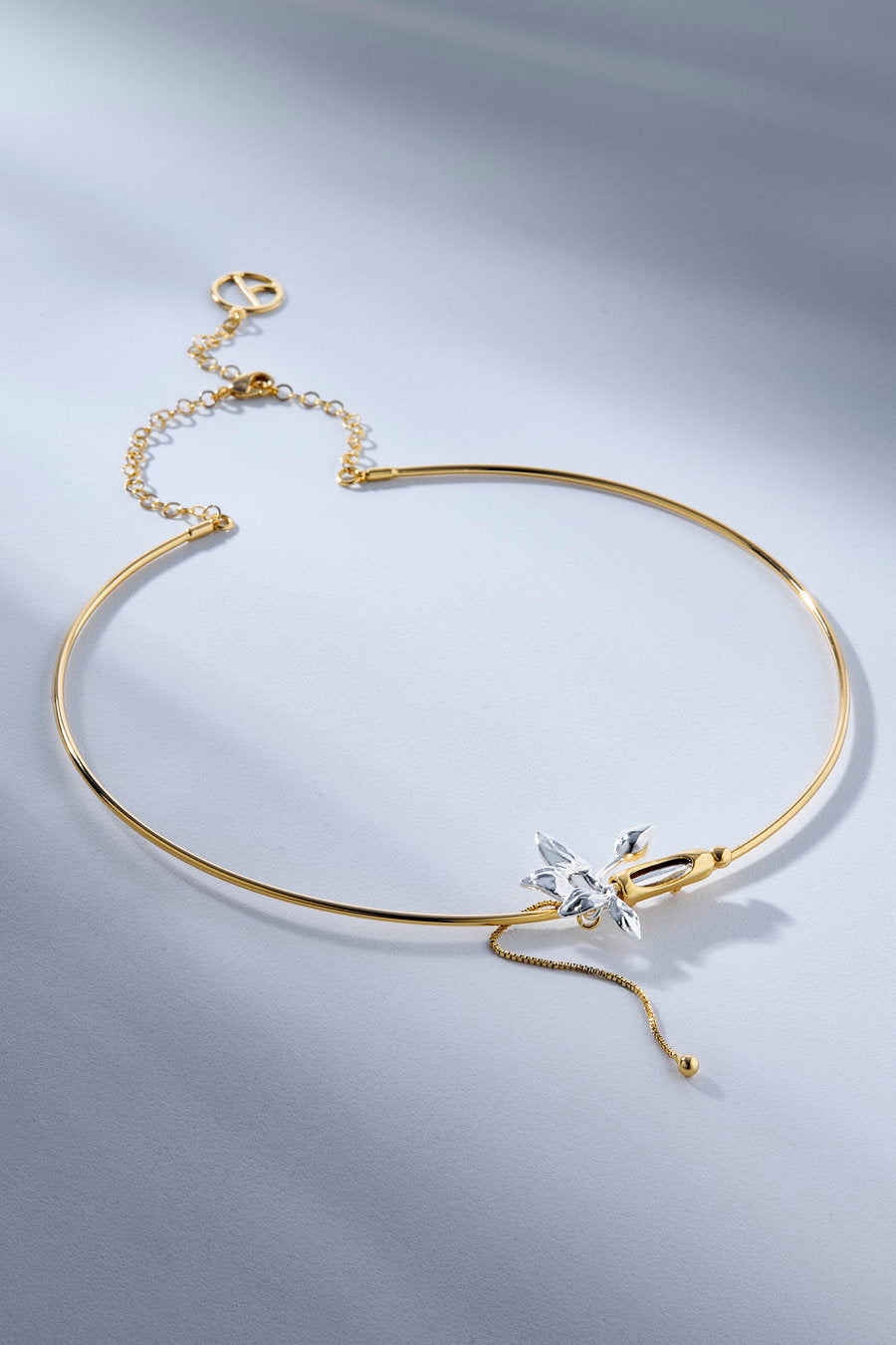A delicate gold bangle necklace with a small silver-toned flower charm set with clear crystals, displayed on a light gray background.