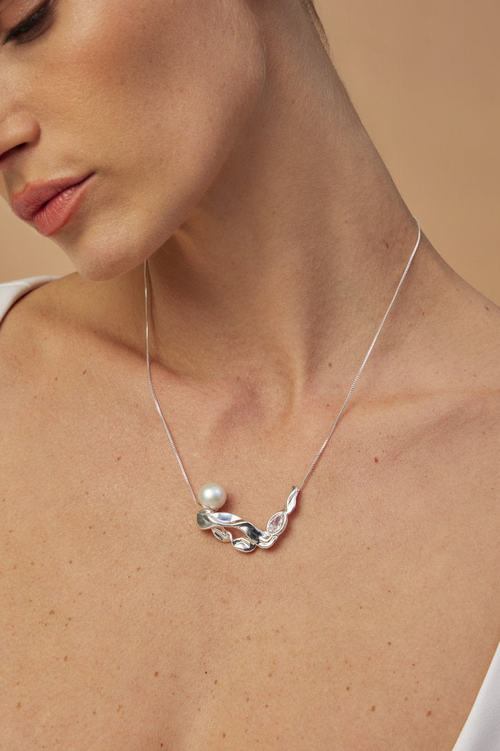 Silver Audrey necklace featuring a sculptural pendant, fluid curves, a pearl, and a faceted crystal.
