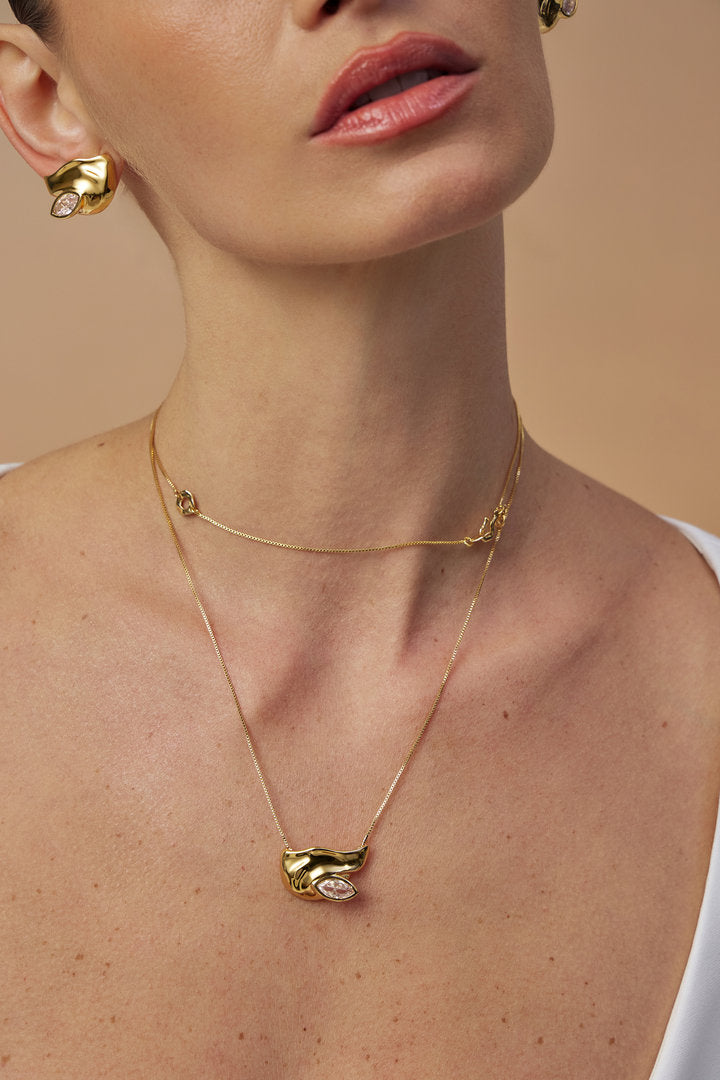 Gold Elsa necklace featuring a delicate chain, an asymmetric pendant, and a uniquely cut crystal.

