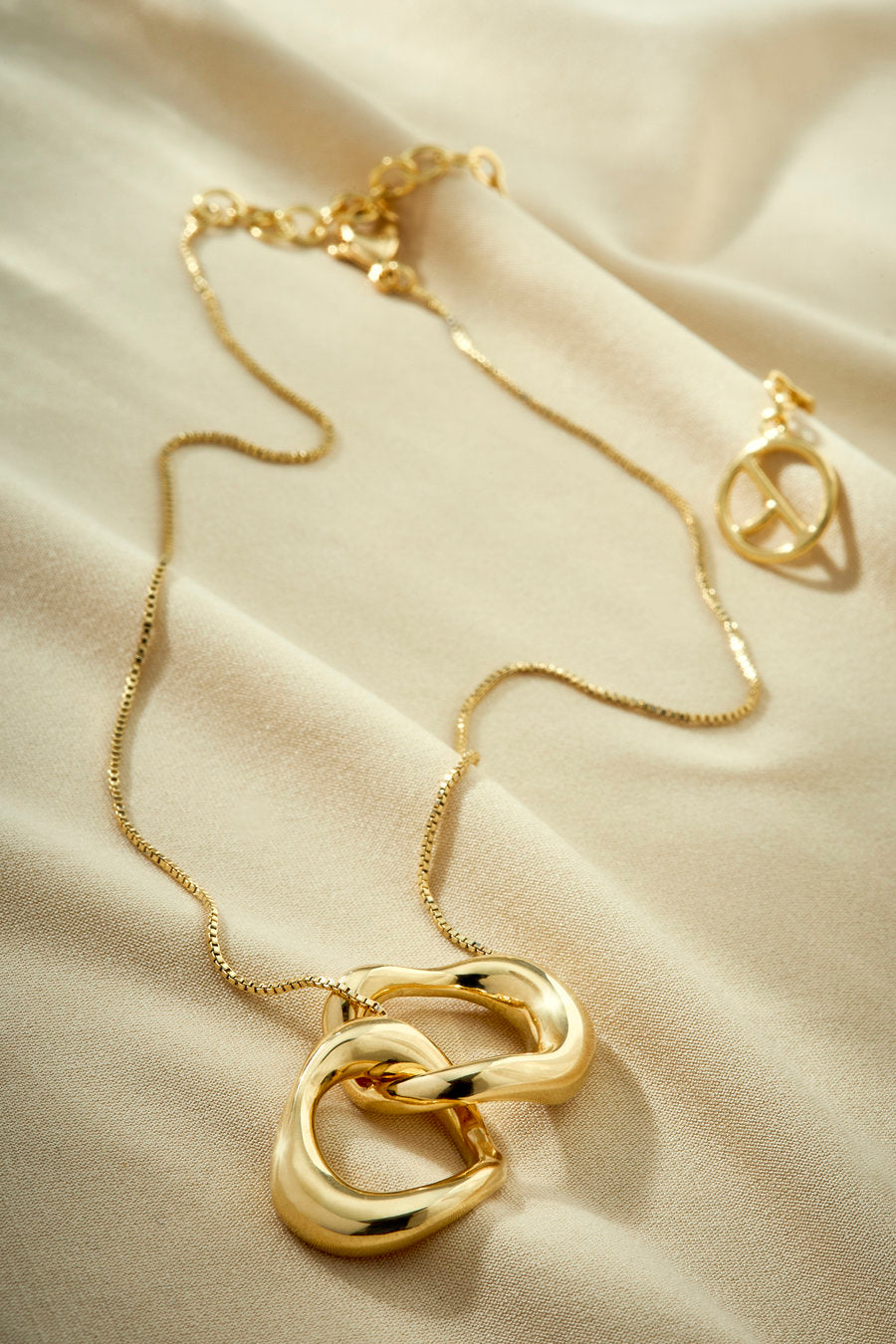Gold necklace with a pendant of intertwined organic links.
