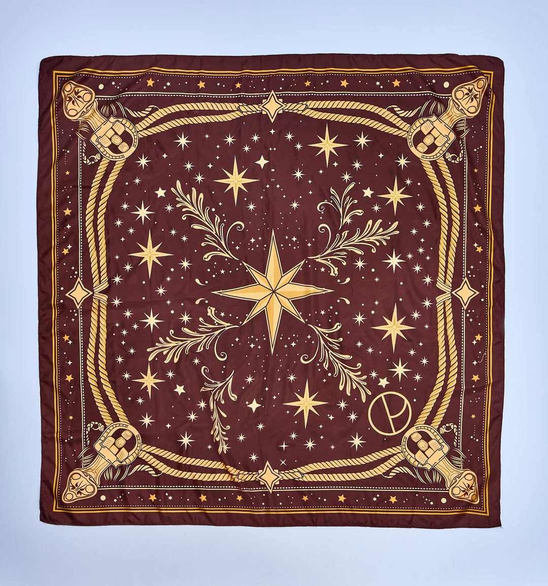 Square burgundy scarf with a gold star print, ornamental cords, arabesques, and a central star inspired by the celestial universe.
