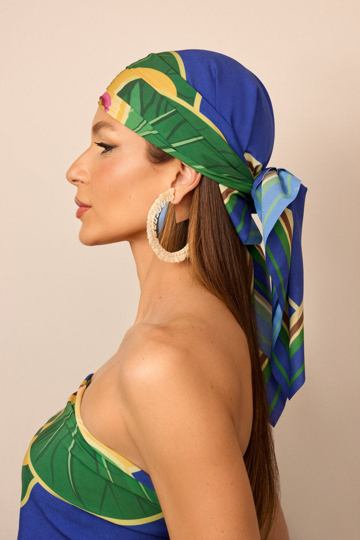 Model wearing a Tropicália headscarf with a vibrant print of orchids and tropical foliage.
